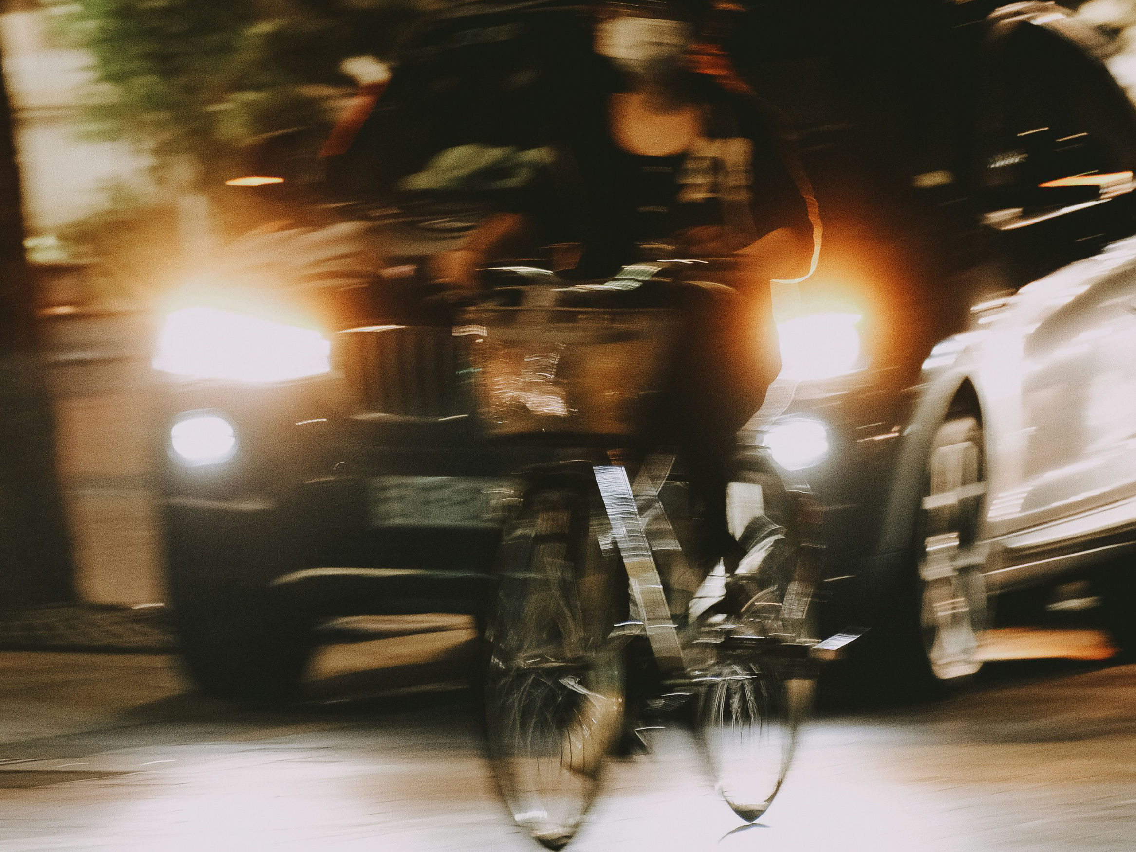 夜間の車道を走る自転車と接近する車